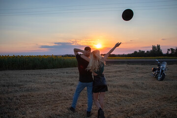 Naklejka premium Bikers man and woman stopped at the side of the road to rest and kiss passionately. Photos of loving motorcyclists at sunset. The concept of freedom, brutality and passion