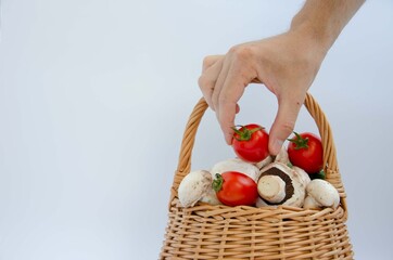 Shopping cart and male hand. Man takes a basket with vegetables and mushrooms. Tomato in hand...