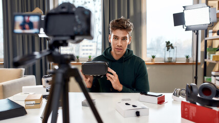 Young male technology blogger recording video blog or vlog review of new vr glasses, headset and other gadgets at home studio. Blogging, Work from Home concept