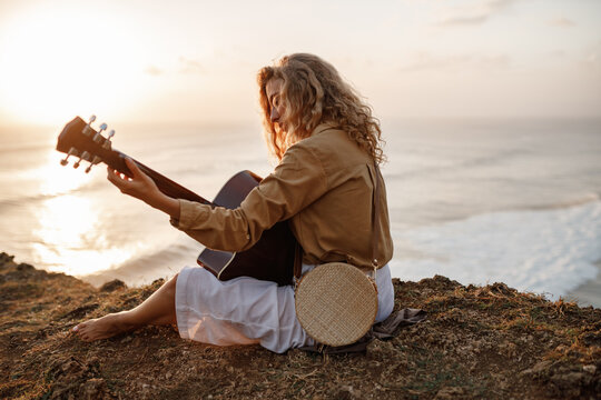 Beautiful young woman playing guitar on the beach, sunset time.  Young woman playing guitar on beach at sunset, back view