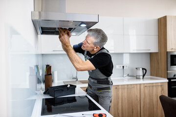 Fixing your technology problem. Aged repairman in uniform working, fixing broken kitchen extractor...