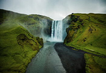View from flying drone. Dramatic midnight sun scene of Skogafoss Waterfall. Aerial summer view of...