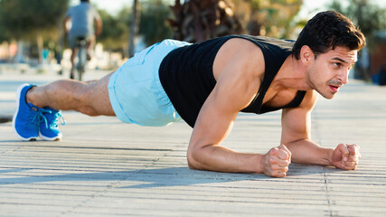 Strong sporty happy positive man doing press exercises holding plank outdoors