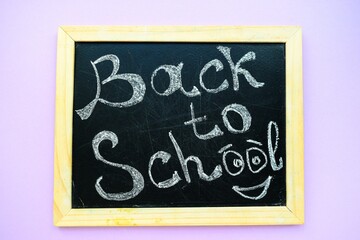 Inscription back to school on a black chalkboard with a wooden frame on a purple background.