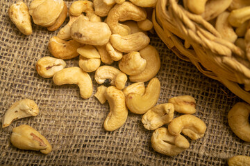 Cashew nuts in a wicker basket and cashew nuts scattered on burlap with a rough texture surface texture. Close up.