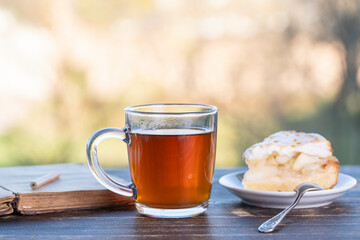 Tea glass with sweet cake and book on wooden table in the morning, outdoors
