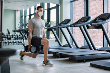 Fototapeta na wymiar Athletic man with face mask having weight training in lunge position in a gym.