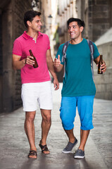 Two male fans are walking with beer and talking outdoor in European city. Focus on right man