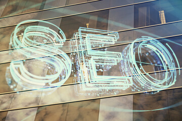 SEO hologram on city view with skyscrapers background double exposure. Search optimization concept.