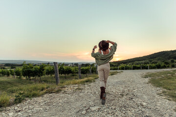 Girl in a cowboy hat at sunset in the countryside in the vineyards.
