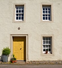 Facade of a house with three, paned windows and pot plants by a bright yellow door
