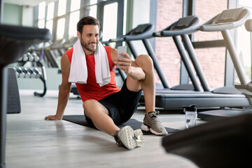 Happy athletic man text messaging on cell phone in health club.