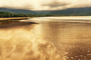 Warmer Sonnenuntergang am Strand von Uvita in Costa Rica mit der Reflexion des Himmels im seichten Wasser © Anna