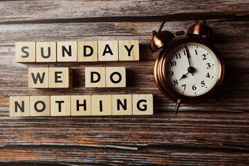 Sunday We do nothing alphabet letter with alarm clock on wooden background;