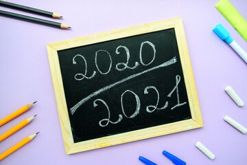 Inscription 2020 2021 chalk on a black chalkboard with a wooden frame on a purple background and stationery.