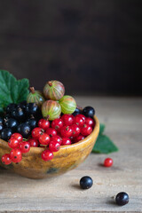 Red and black currant, gooseberry in ceramic bowl on a wooden background