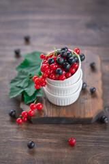 Red and black currant berries in ceramic bowl on a wooden background