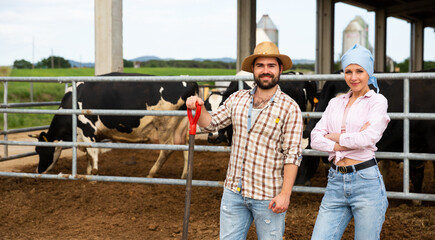 Positive female and man farmers standing during break at cow farm