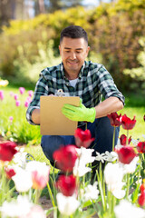 gardening and people concept - happy smiling middle-aged man writing to clipboard and taking care of flowers at summer garden