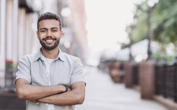 Handsome smiling young man portrait. Cheerful men with crossed arms looking at camera in city. People concept