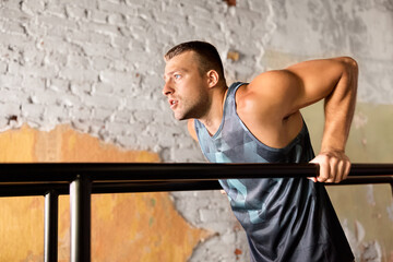 fitness, sport, bodybuilding and people concept - young man doing triceps dip exercise on parallel bars in gym