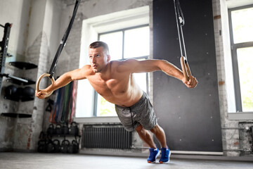 fitness, sport, bodybuilding and people concept - young man exercising on gymnastic rings in gym
