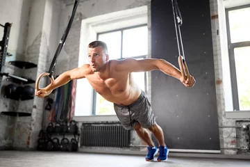 Schilderijen op glas fitness, sport, bodybuilding and people concept - young man exercising on gymnastic rings in gym © Syda Productions