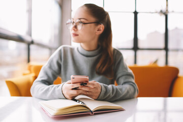 Obraz premium Selective focus on modern smartphone in hand of female student chatting with friends in networks and dreaming about weekend.Blurred businesswoman looking away in window downloading files on mobile