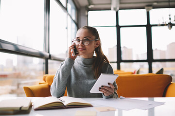 Serious female entrepreneur in eyeglasses having phone conversation about startup project...