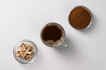 A healthy drink, an alternative to coffee. Chicory drink in a glass cup, dried roots and powder in bowls on a light gray stone background. Top view, space for text.