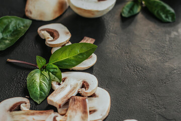 Champignon slices and basil leaves on a black background copy space.