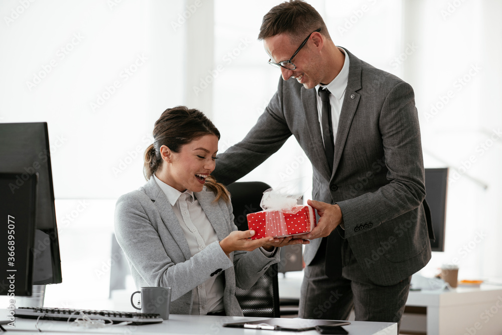 Wall mural young businessman giving his colleague present in office. young man suprise beautiful businesswoman 