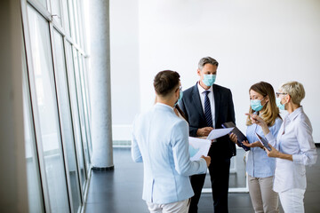 Business partners standing and looking at business results in office while wearing face masks sa an virus protection