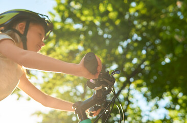 Happy teenager girl rides best bike on a summer sunny day in a city park. Against the background of green leaves of trees. Urban biking - teen and bike in city park. Close up photo.