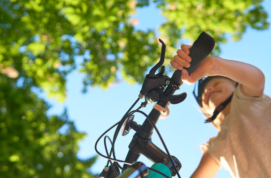 Little caucasian girl with blond hair rushes on a bicycle on a sunny summer day. View from the bottom. Focus on the hand. Urban biking - teen and bike in city park.