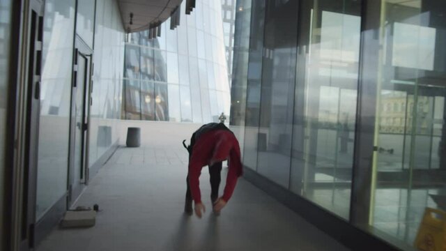 Back view following shot of young man running though walk way between urban buildings, performing front flip, cartwheel and backflip while practicing parkour and freerunning outdoors - Powered by Adobe