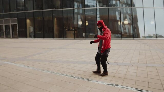 Young male athlete in sportive outerwear and neck warmer over his face performing backflip while practicing parkour outdoors in the city