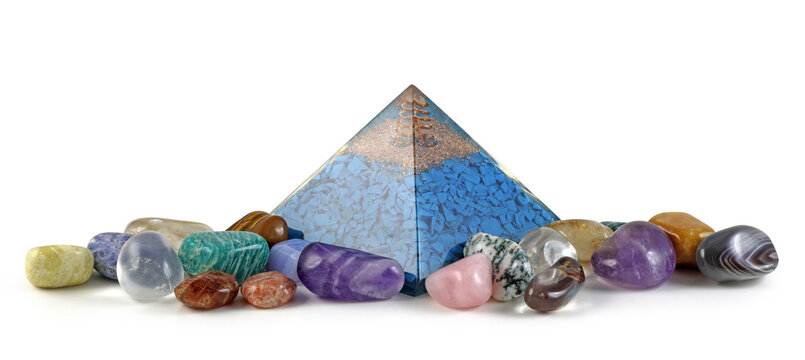 Orgone pyramid power and healing crystals - copper spiral and clear quartz on top of blue chip stones inside Orgone pyramid surrounded by mixed tumbled healing stones isolated on white background

