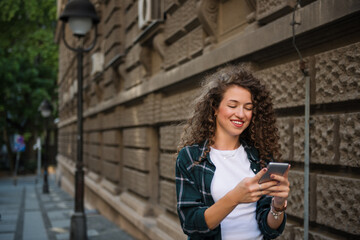 Beautiful young woman walking on the street and using smart phone