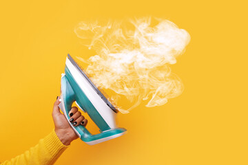 modern iron with steam in hand over yellow background