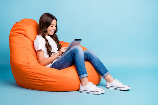 Portrait of nice attractive cheerful cheery focused wavy-haired girl sitting in chair using tablet ebook isolated on bright vivid shine vibrant blue teal turquoise color background