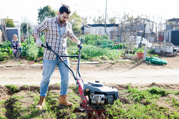 Man professional gardener using plow at land with green grass in garden outdoor