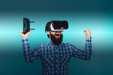 bearded man rejoices victory in glasses of virtual reality over blue background
