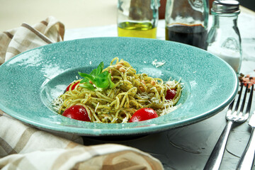 Italian pasta spaghetti with pesto sauce and tomatoes in a blue plate in a composition with kitchen utensils