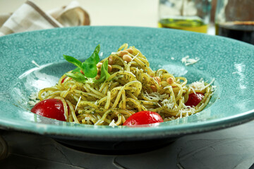 Italian pasta spaghetti with pesto sauce and tomatoes in a blue plate in a composition with kitchen utensils