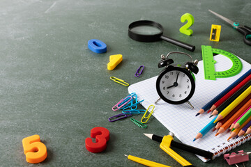 Back to school and education concept with small alarm clock, paper notebook and school supplies on blackboard background..