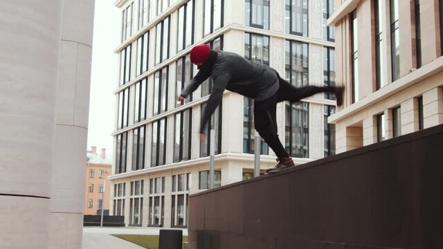 Slow motion tilt down shot of male parkour athlete performing front flip off urban ledge while training outdoors in city downtown