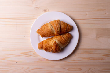 a white ceramic cup with black espresso, french croissant as breakfast or snack concept on rustic, natural texture wooden surface