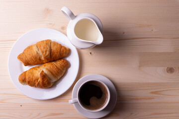 a white ceramic cup with black espresso, french croissant as breakfast or snack concept on rustic, natural texture wooden surface