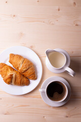 a white ceramic cup with black espresso, french croissant as breakfast or snack concept on rustic, natural texture wooden surface